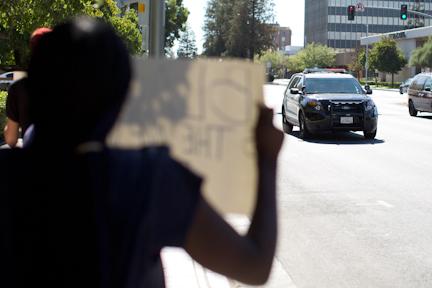 A protestor shows a sign to a passing Bakersfield Police department cruiser as he drives by the scene. AJ Alvarado/The Runner