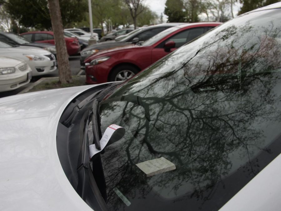 A student receives a ticket while displaying their parking pass receipt number on a sticky note. Photo by Ray Alarcon Marquez / The Runner