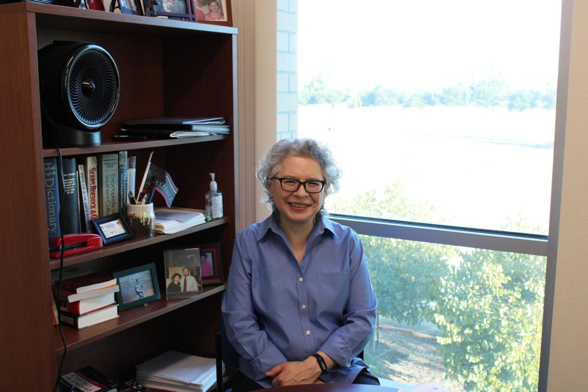 Dean Rodriquez smiling for a photo, as she is seated at the round table in her office. 
Photo by Raul Rico/The Runner